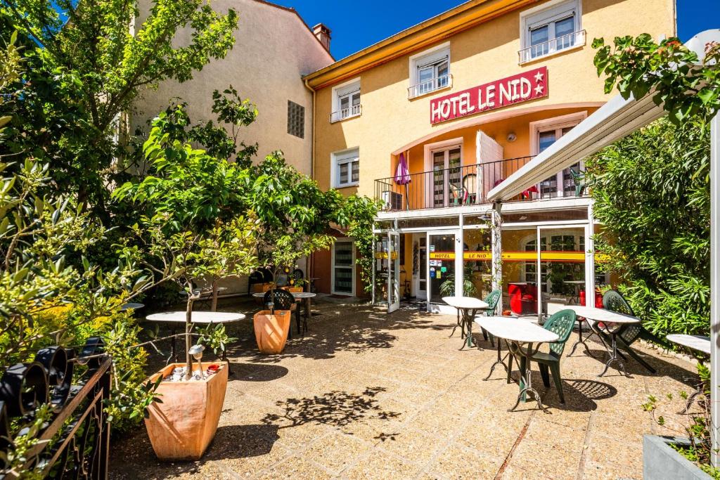 un patio avec des tables et des chaises en face d'un bâtiment dans l'établissement Hôtel le Nid, à Argelès-sur-Mer