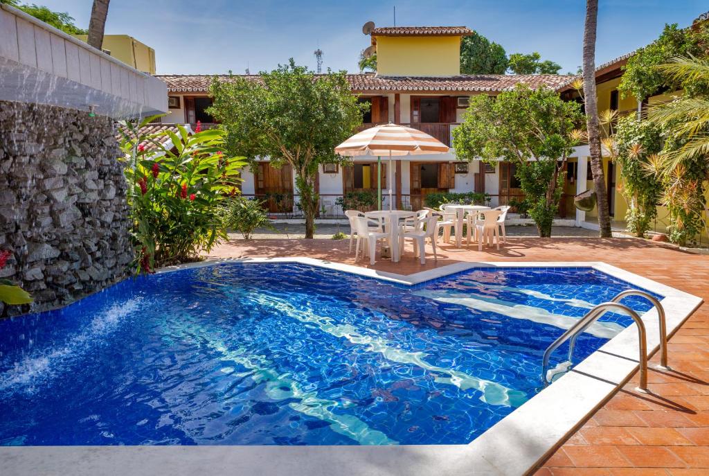 uma piscina com mesa e cadeiras e uma casa em Chauã Porto Hotel em Porto Seguro