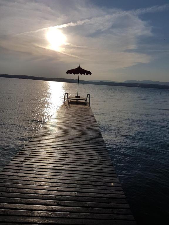 a bench on a dock with an umbrella on the water at Residence Alexandra Stay in Sirmione