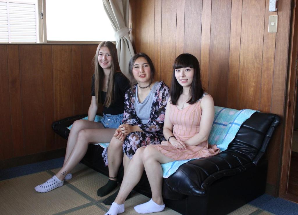 three girls are sitting on a leather couch at 磯ノ浦駅前ゲストハウス 月と空moon and sky in Wakayama