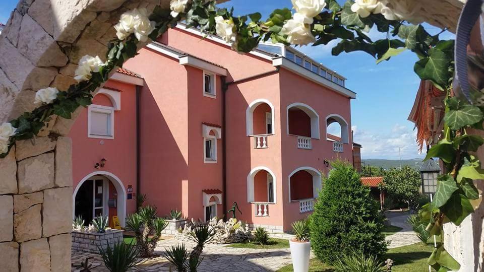een groot roze gebouw met witte ramen en planten bij B&B Villa La Perla in Punat