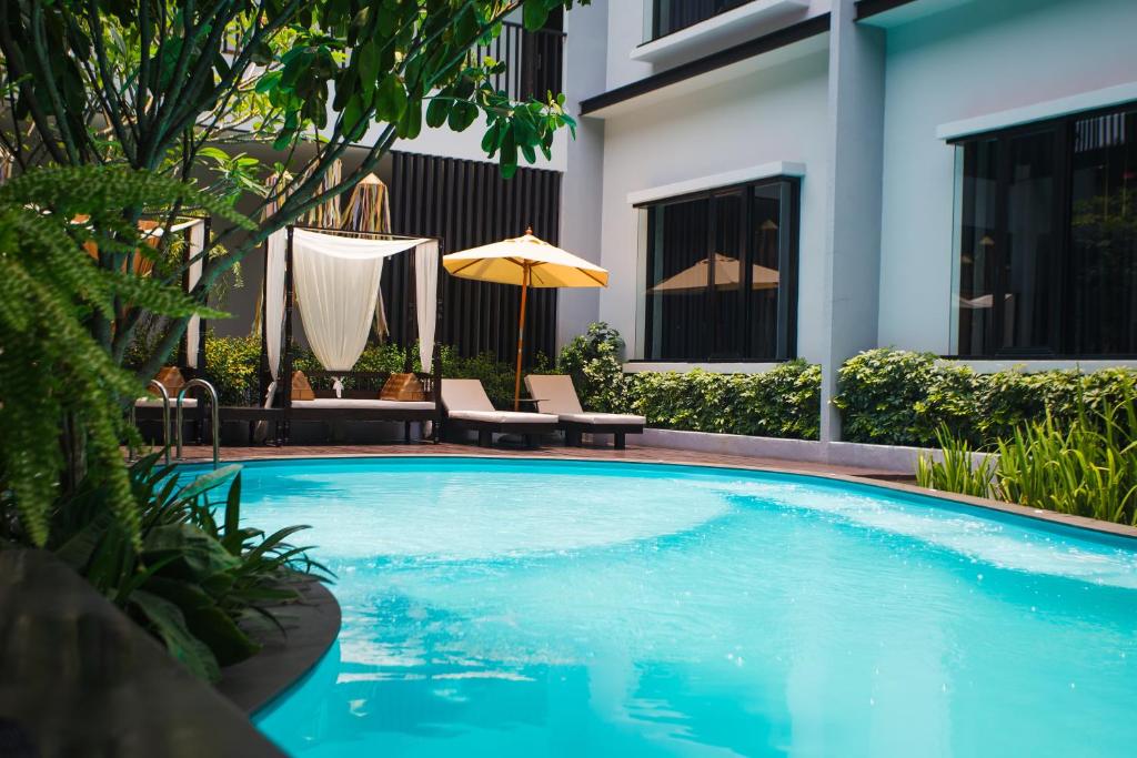 a swimming pool with chairs and an umbrella next to a building at NAI YA Hotel -SHA Extra Plus in Chiang Rai