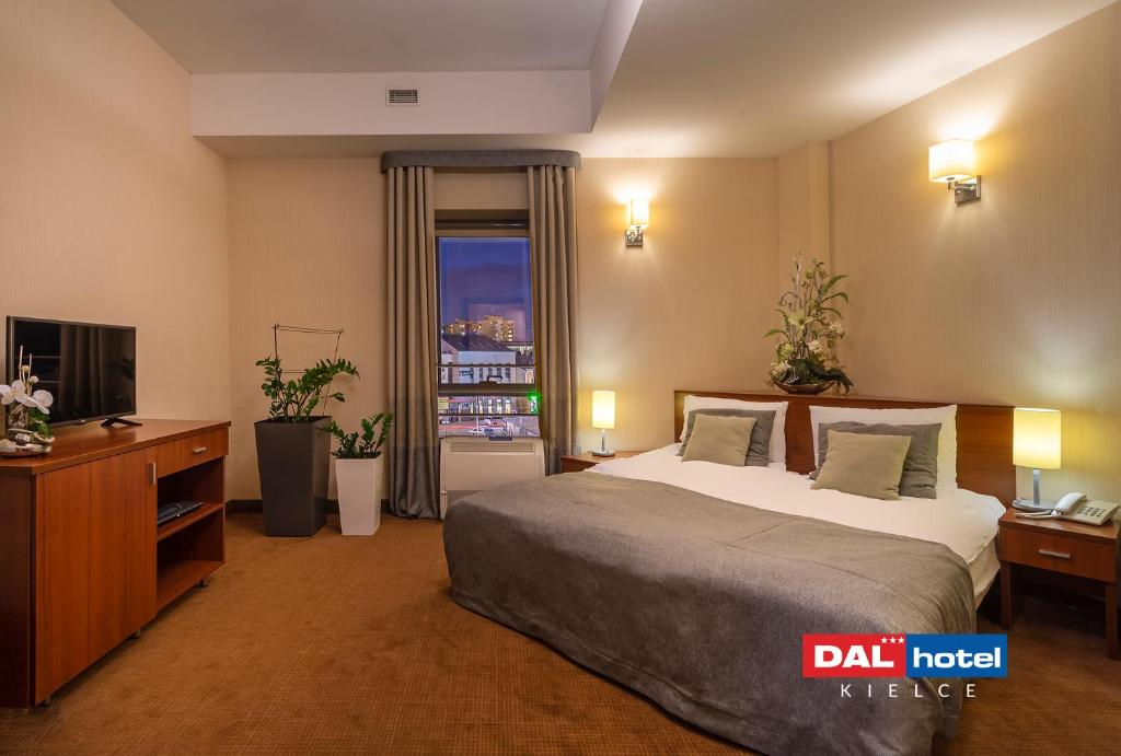Spacious hotel bedroom with king-size bed, gray linens, bedside lamps, TV cabinet and evening city view.