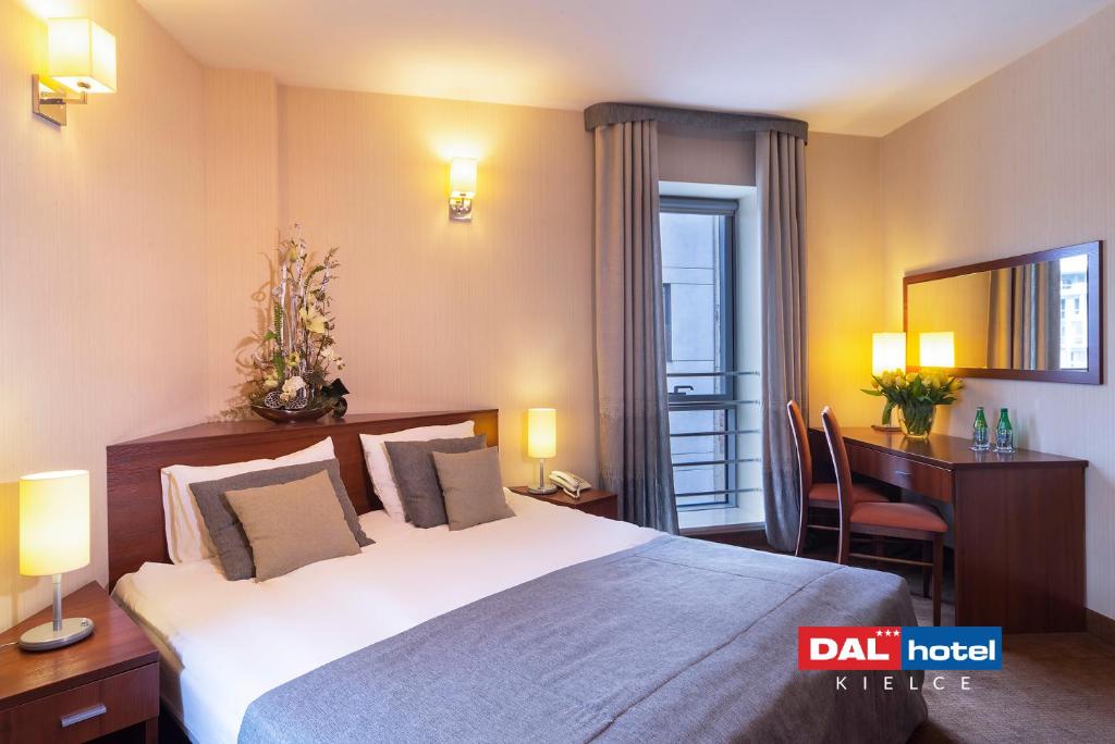 Cozy hotel bedroom with large bed, decorative cushions, bedside lamps, desk and window.