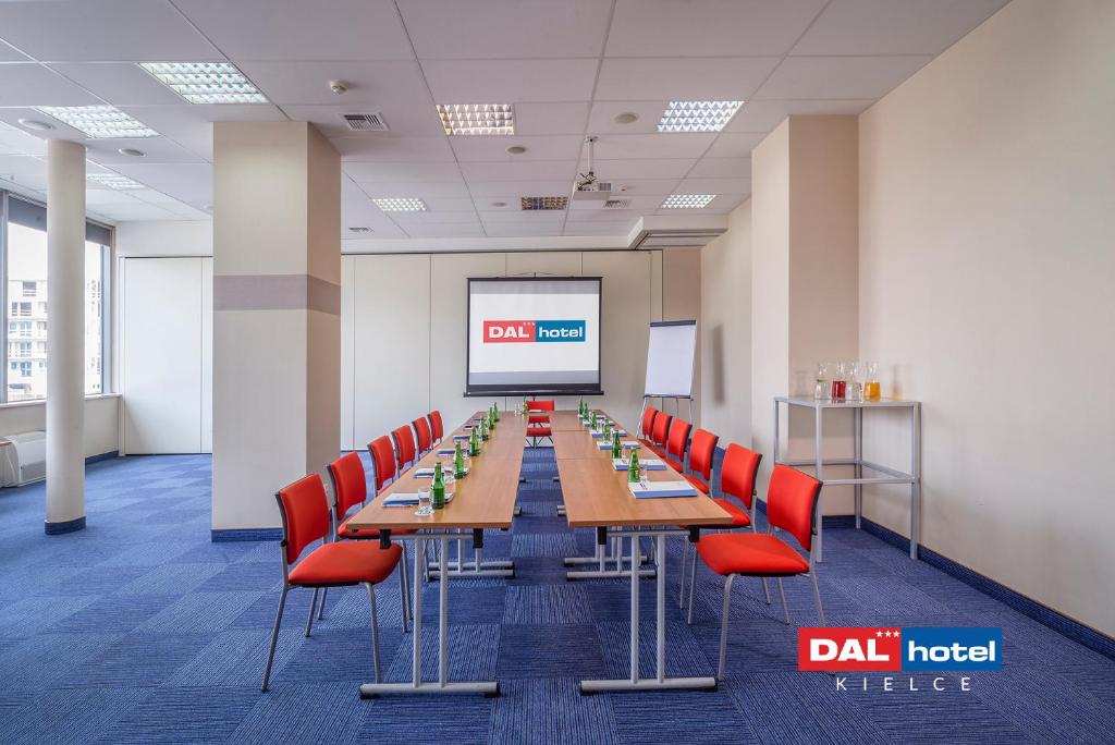 U-shaped meeting setup with long tables, red chairs, projector screen, bottled water and folders.