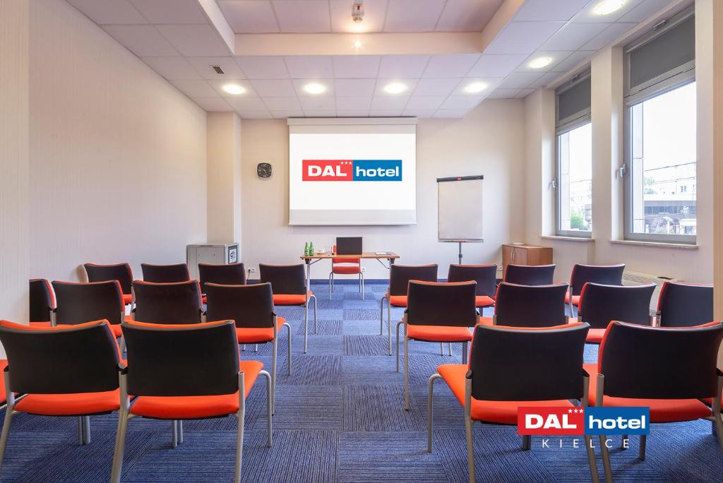 Presentation room with rows of orange chairs facing a projector screen, bright windows.