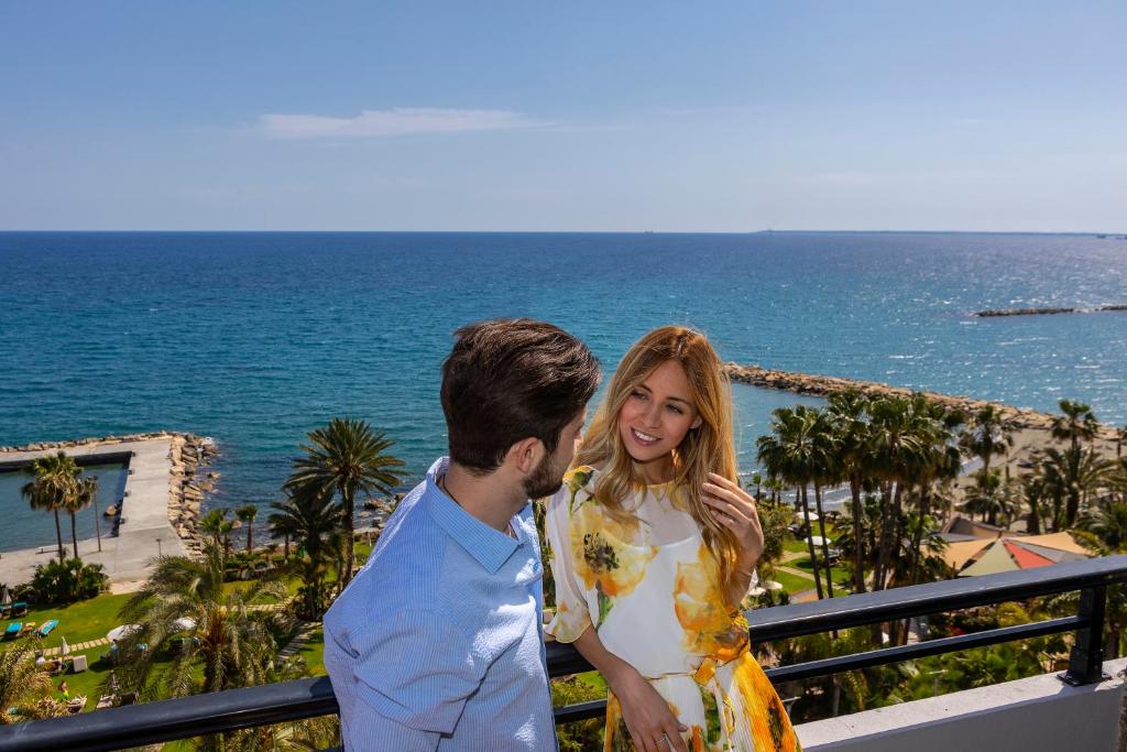 a man and a woman standing on a balcony overlooking the ocean at Amathus Beach Hotel Limassol in Limassol