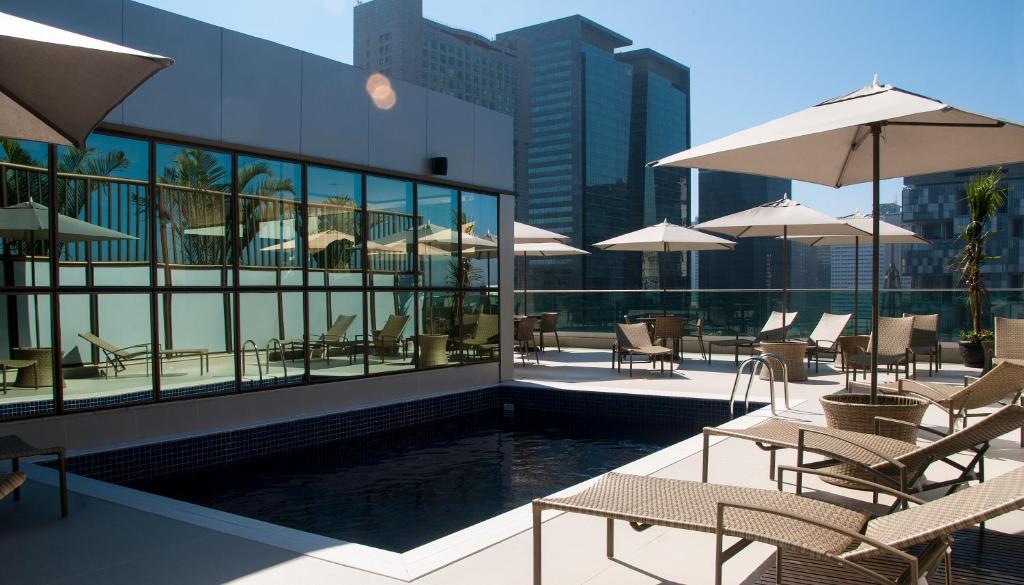 uma piscina com cadeiras e guarda-sóis num edifício em Américas Granada Hotel no Rio de Janeiro