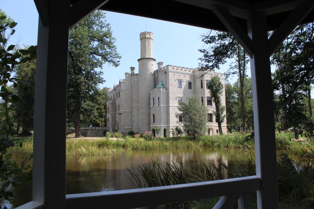 View of stately castle across a pond framed by a wooden gazebo, summer greenery