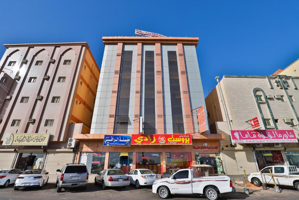 un edificio alto con coches estacionados frente a él en فواصل تبوك Fawasel Tabuk, en Tabuk