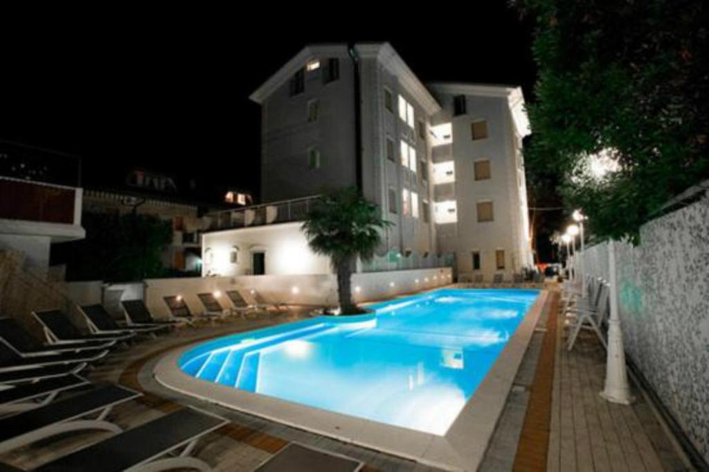 una piscina con sedie e un edificio di notte di Hotel San Carlo Cesenatico a Cesenatico