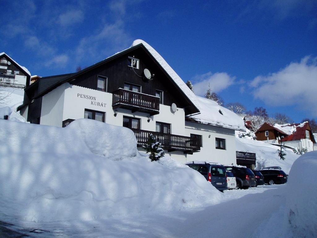a building covered in snow with cars parked in front at Pension Kubát in Špindlerův Mlýn