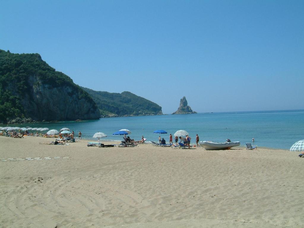 a group of people on a beach with umbrellas at Holiday Studio Apartments yannis on the beach of Agios Gordios in Corfu in Agios Gordios