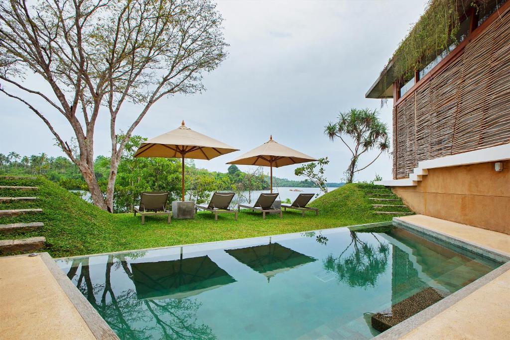 a pool with chairs and umbrellas next to a house at Tri by Amaya in Ahangama