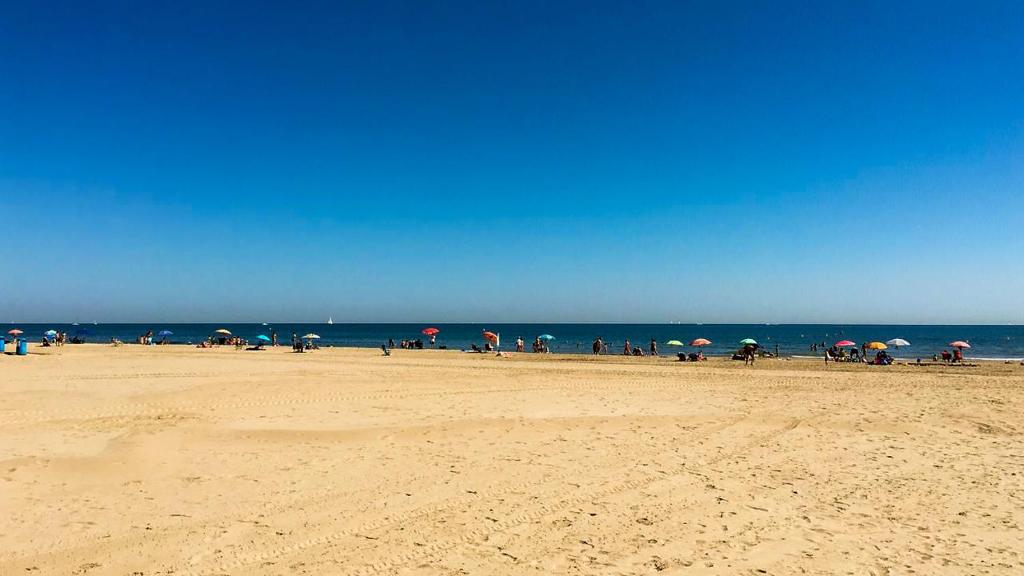 a group of people standing on a beach with umbrellas at 250 Playa in Puerto de Sagunto