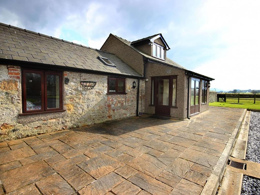 a stone house with a patio in front of it at Barras Cottage in Dwyran