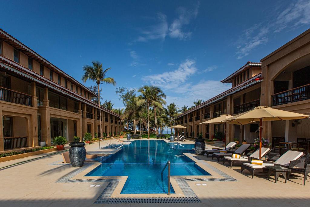 a swimming pool with chairs and umbrellas next to a building at Marquis Beach Resort in Candolim