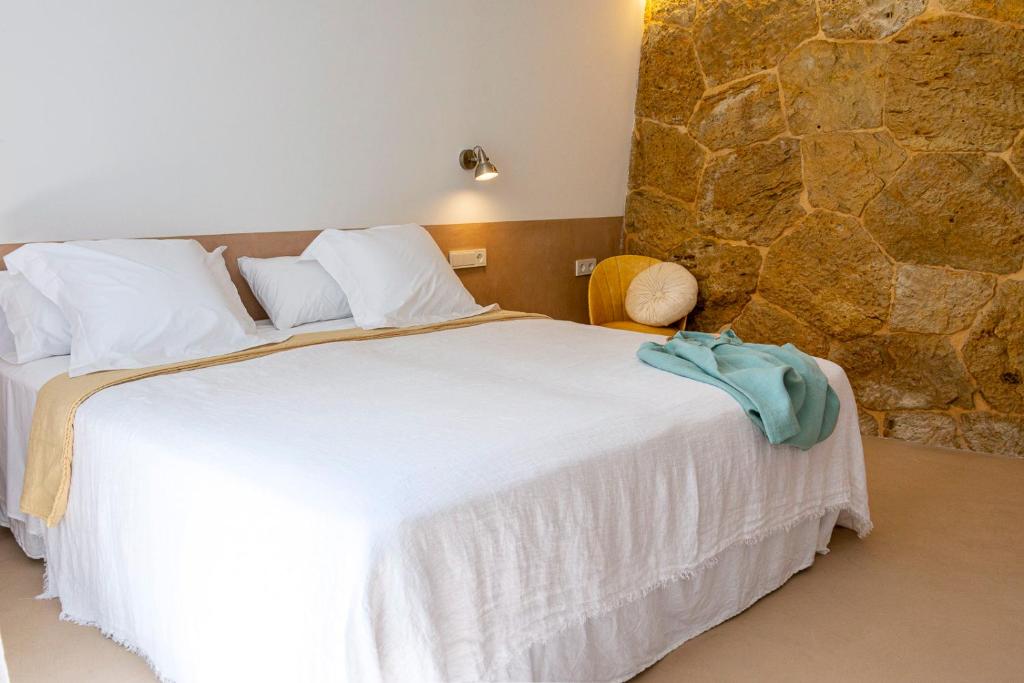 a bedroom with a large white bed with a stone wall at Noualt in Ferreries