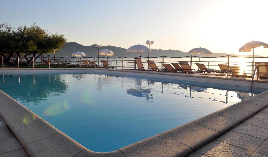 a large swimming pool with chairs and the ocean at Hotel Tettola in Saint-Florent
