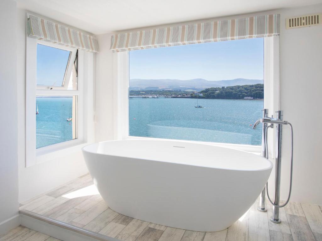 uma banheira branca na casa de banho com uma grande janela em Glan Dwr Bach em Llandegfan