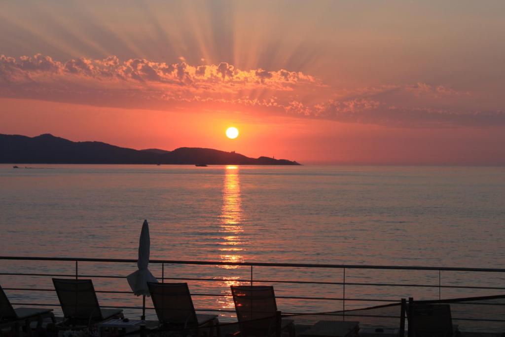 a sunset view of the ocean with a sailboat in the distance at Hotel Tettola in Saint-Florent