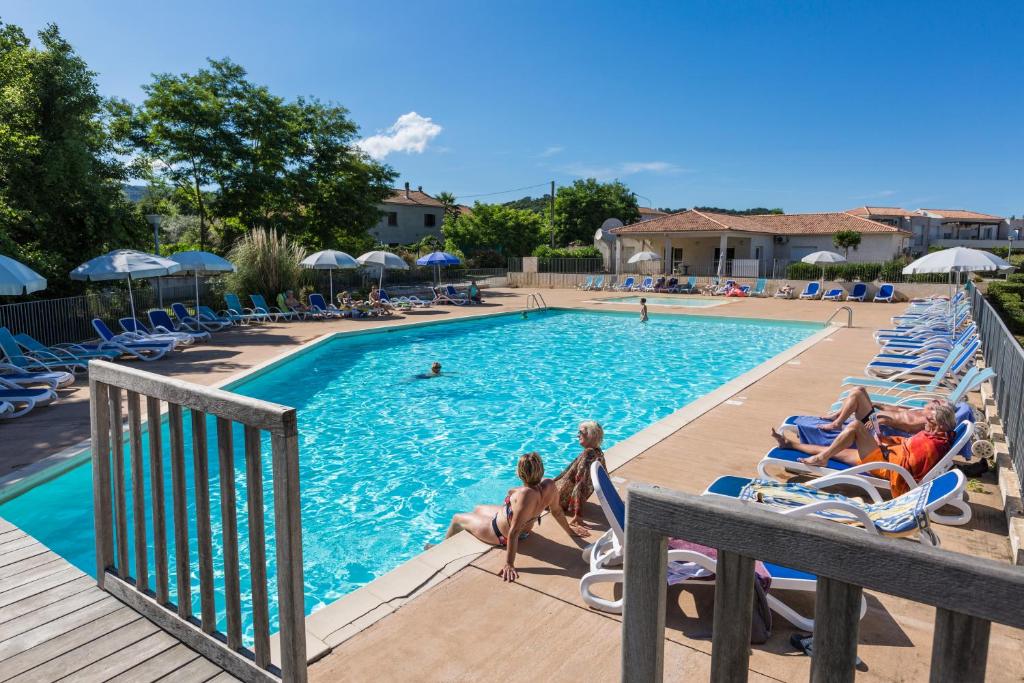 una piscina in un resort con persone sedute su sedie a sdraio di Résidence Odalys Acqua Bella a Poggio-Mezzana