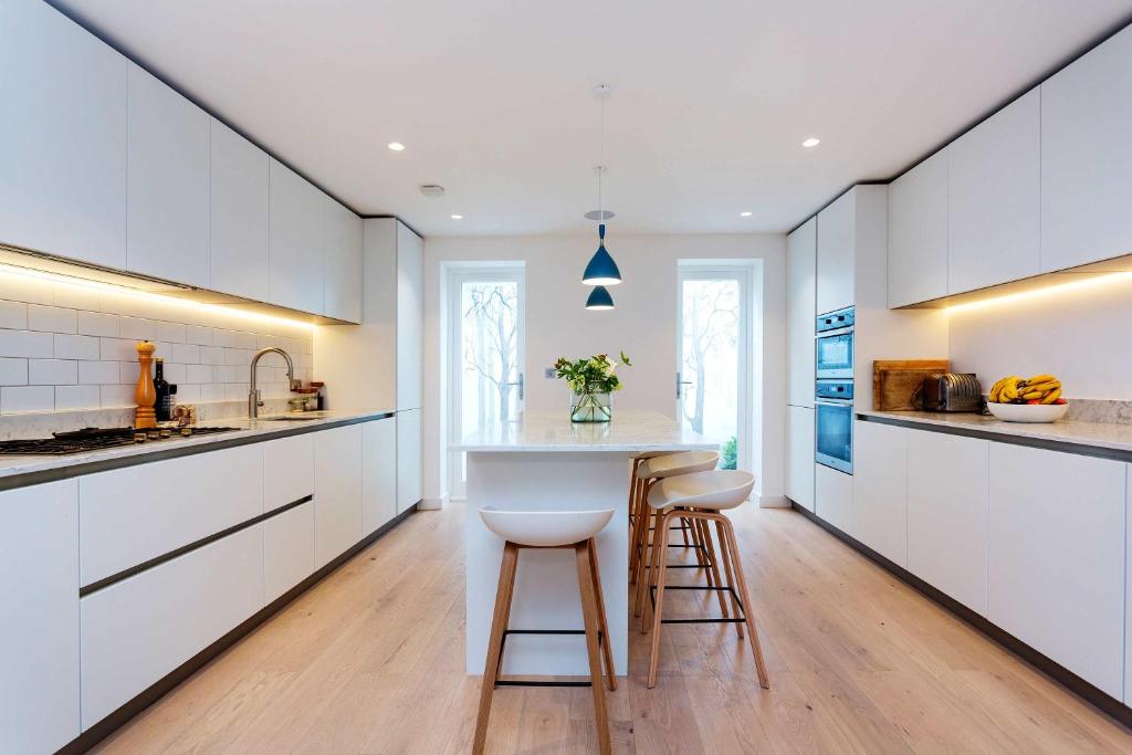 a kitchen with white cabinets and a island with stools at Veeve - Princedale Road Minimalism in London