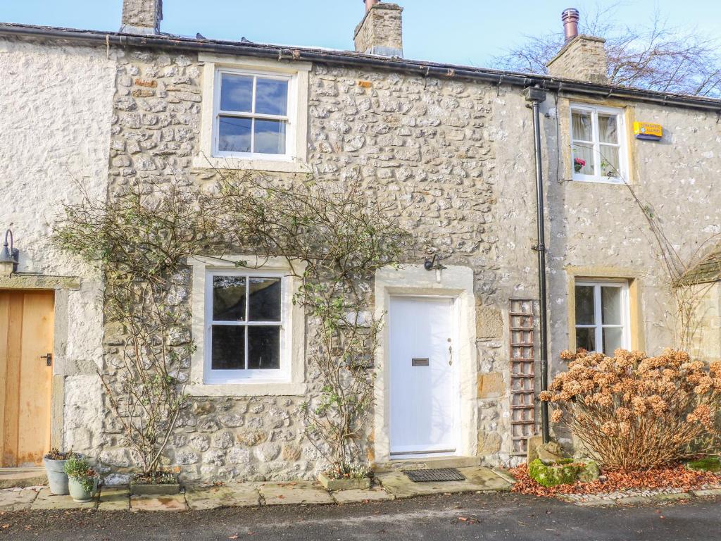 ein altes Steinhaus mit einer weißen Tür in der Unterkunft Rose Cottage in Skipton
