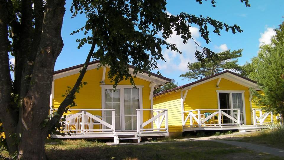 une maison jaune avec une véranda et un arbre dans l'établissement Poilsio Nameliai Oazė, à Šventoji