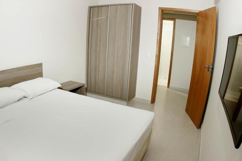 a bedroom with a white bed and a wooden cabinet at Prive Atrium Thermas Residence in Caldas Novas