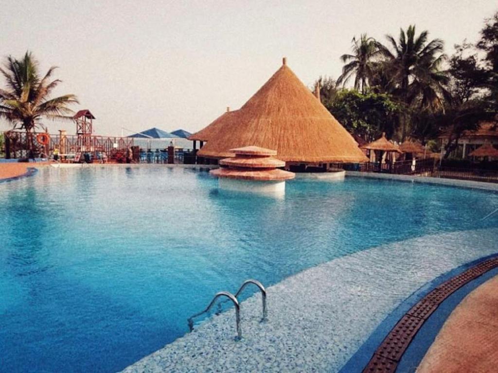 a large swimming pool with a straw building in the background at Senegambia Beach Hotel in Sere Kunda NDing