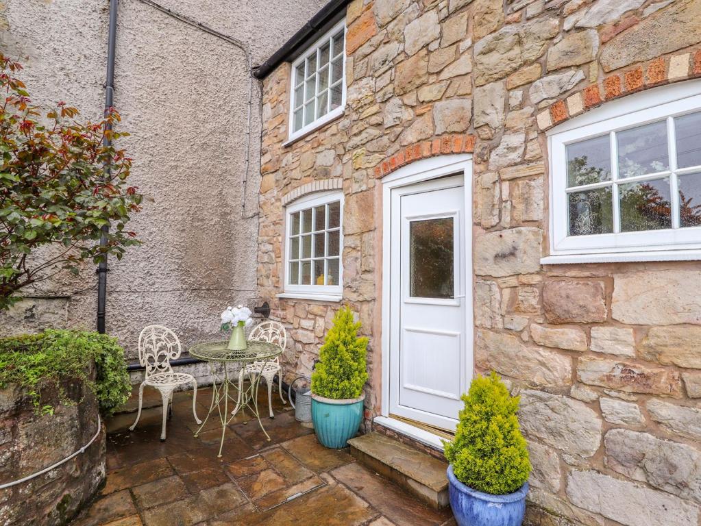 een stenen huis met een witte deur en een tafel en stoelen bij Woodland Cottage in Llangollen