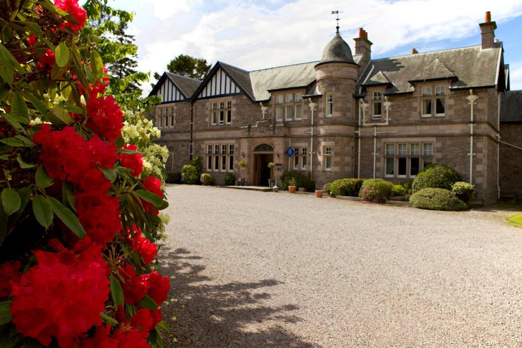 an old house with red flowers in front of it at Ramnee Hotel in Forres