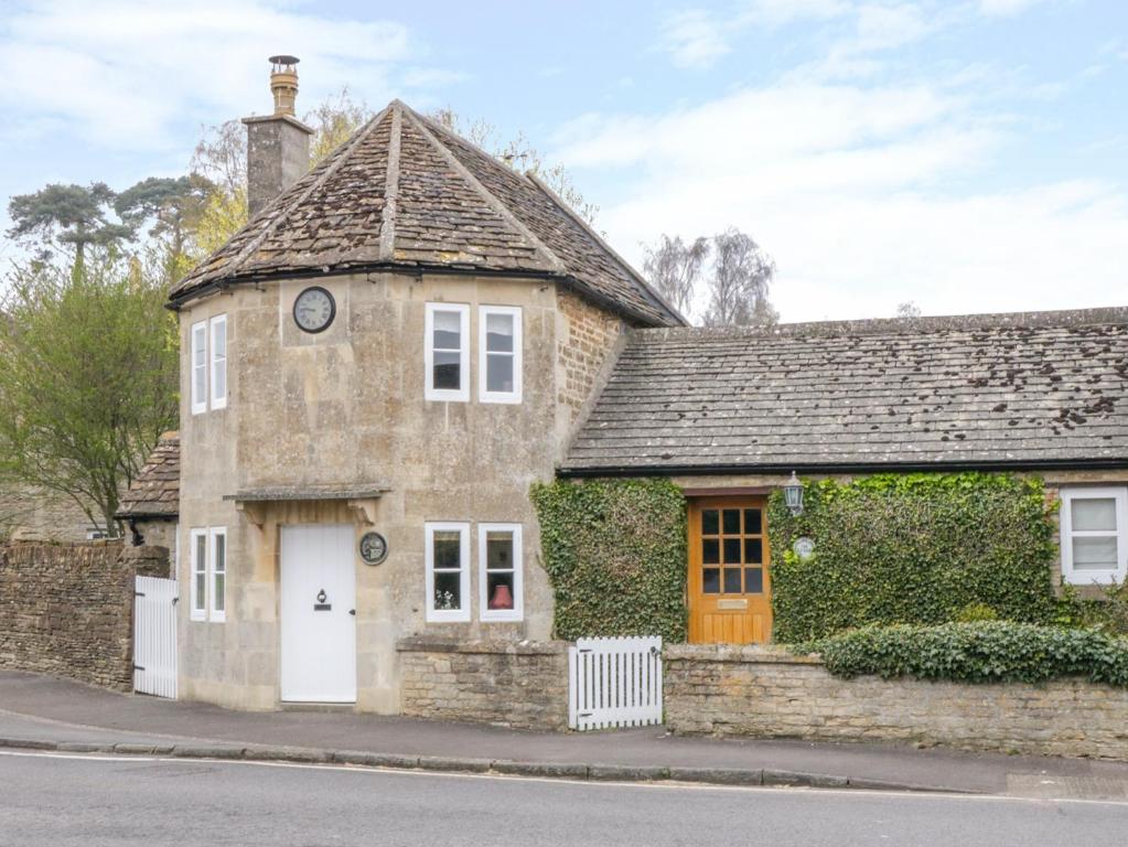 een oud stenen huis met een klok op het dak bij Pike Cottage in Acton Turville