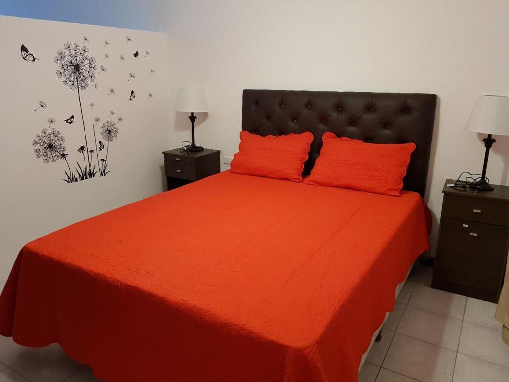 1 dormitorio con 1 cama roja y 2 almohadas de color naranja en departamento centro en La Rioja