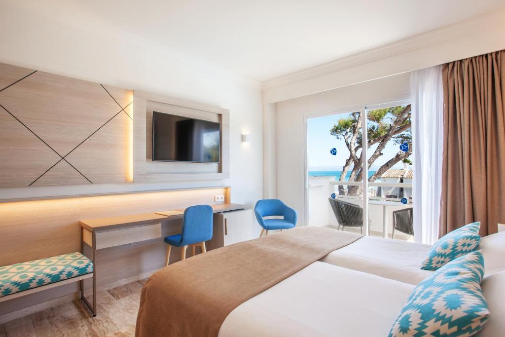 a hotel room with a bed and a desk and a window at Grupotel Los Príncipes & Spa in Playa de Muro