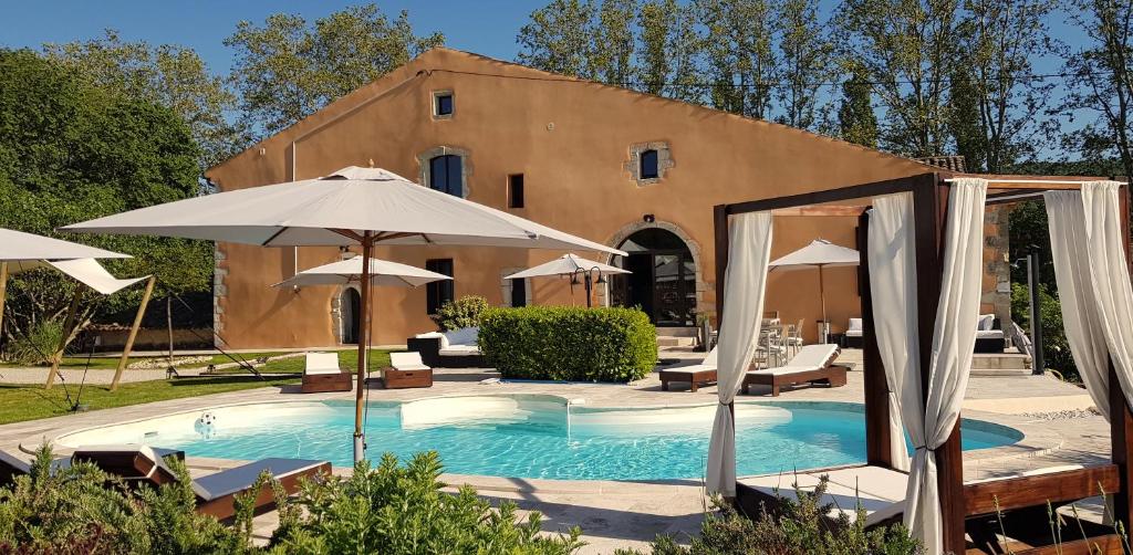 a swimming pool with umbrellas and a building at Domaine De Pradaous in Reillanne