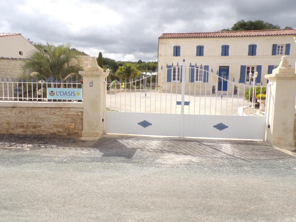 uma cerca branca com um portão em frente a um edifício em L'Oasis em Port-dʼEnvaux
