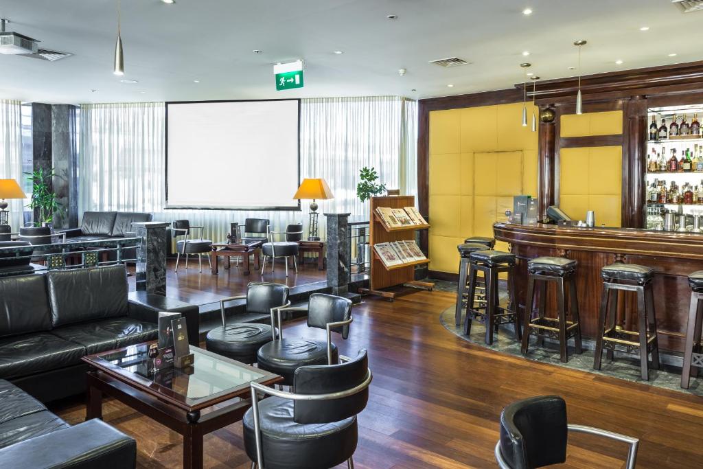 A polished hotel lounge and bar with leather seating, a large screen, and a stocked back bar.