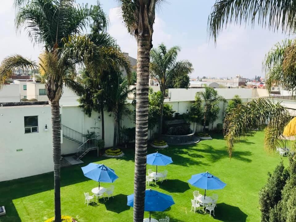 a yard with palm trees and blue umbrellas at Hotel Posada Maria Sofia in Cholula