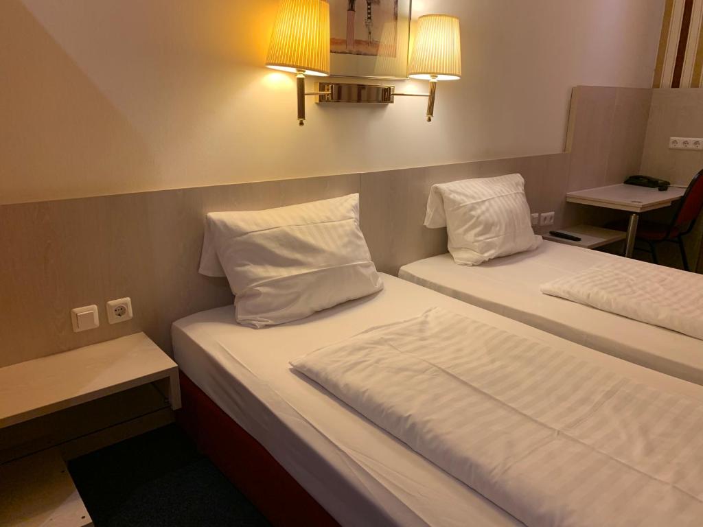 two beds in a hotel room with white sheets and pillows at Hotel New Fair Munich Messe in Munich