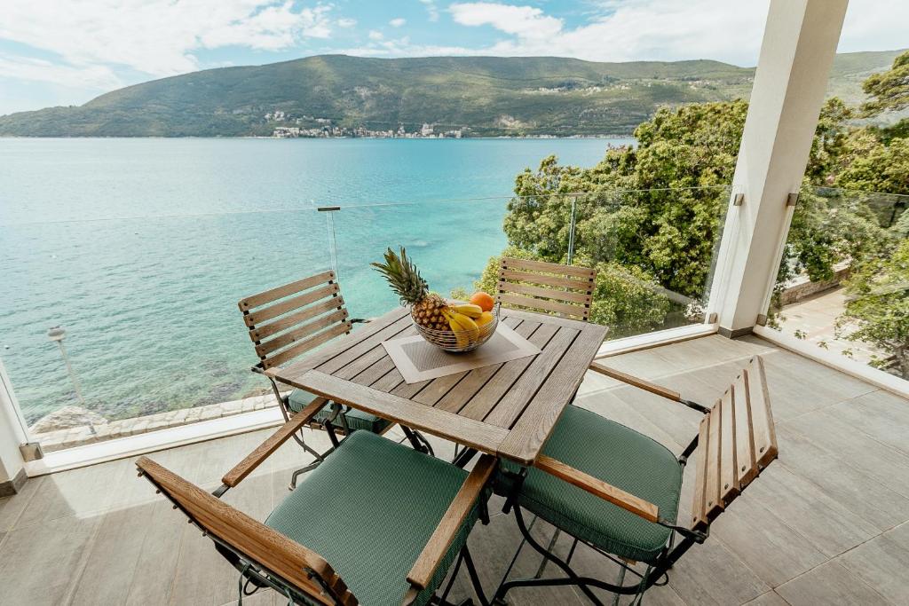 drewniany stół z krzesłami i miska owoców na balkonie w obiekcie Apartments Joy w mieście Herceg Novi