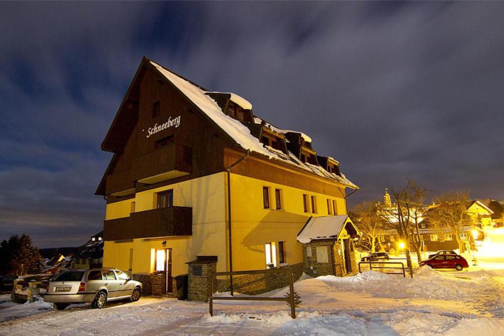 a large yellow building in the snow at night at Schneeberg Apartmany in Boží Dar
