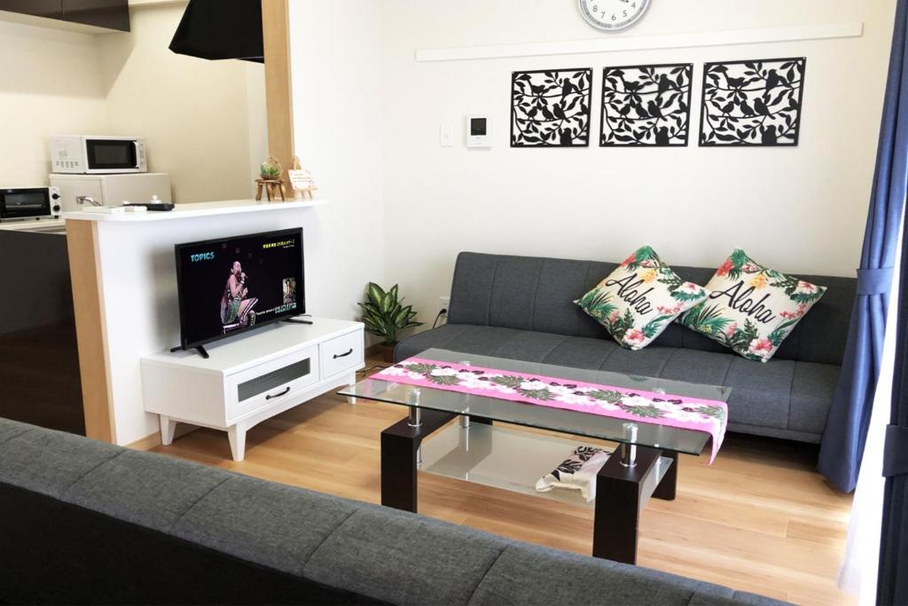 ein Wohnzimmer mit einem Sofa, einem Tisch und einem TV in der Unterkunft TerraceRin YN14 in Tomigusuku