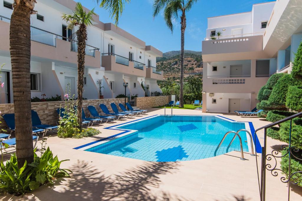 a swimming pool in front of a building with palm trees at Emerald Hotel in Malia