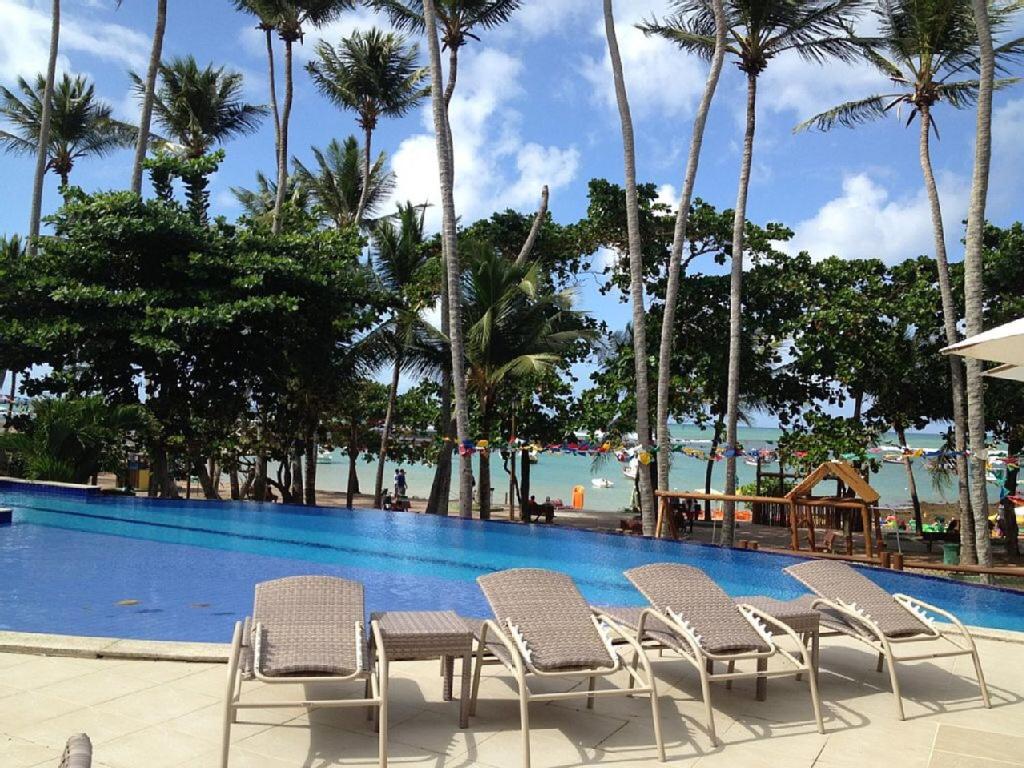 a pool at a resort with chairs and palm trees at Praia do Forte - Frente ao Mar in Praia do Forte