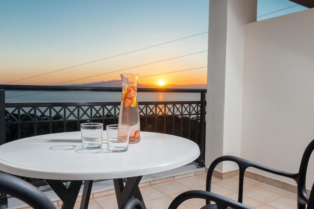 a white table with two glasses on a balcony with the sunset at Hotel Villa Natassa in Skala Rachoniou