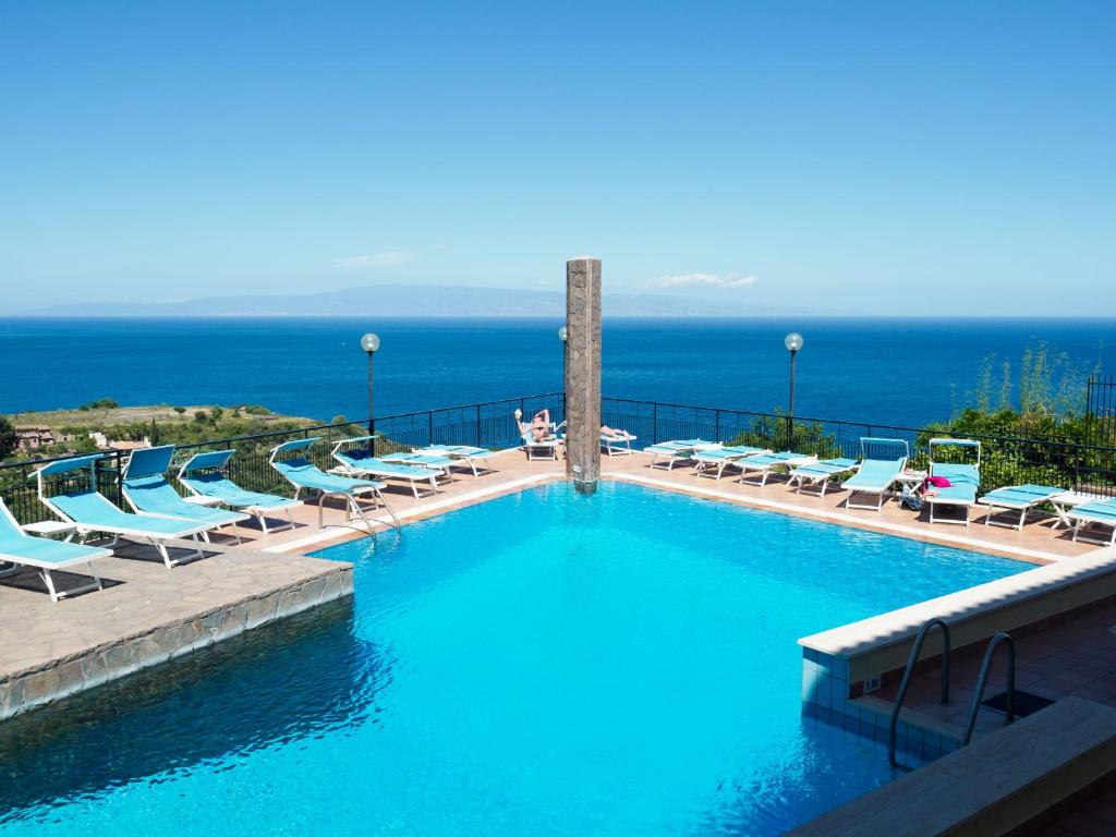 a large swimming pool with lounge chairs and the ocean at Hotel Sirius in Taormina