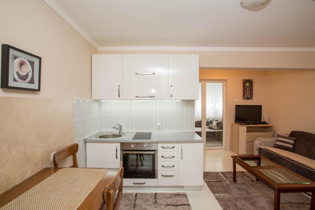 a kitchen with white cabinets and a living room at Valentina Apartman in Petrovac na Moru