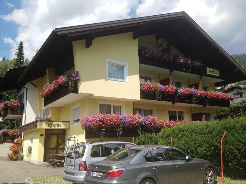 two cars parked in front of a yellow building with flowers at Pension & Appartement Fortin in Bad Kleinkirchheim